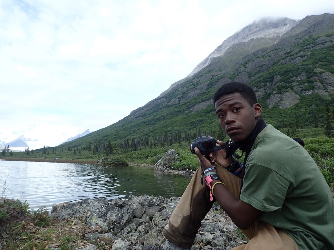 A young man taking a picture of a mountain.