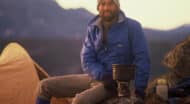 A man sitting on top of a mountain with a cup of coffee.
