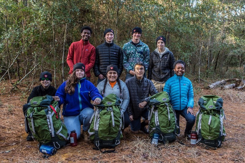 A group of people posing with backpacks in the woods.