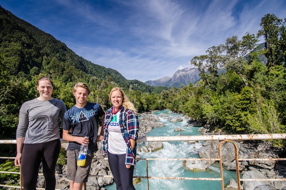Three people smiling with a view of a river and mountains in the background.