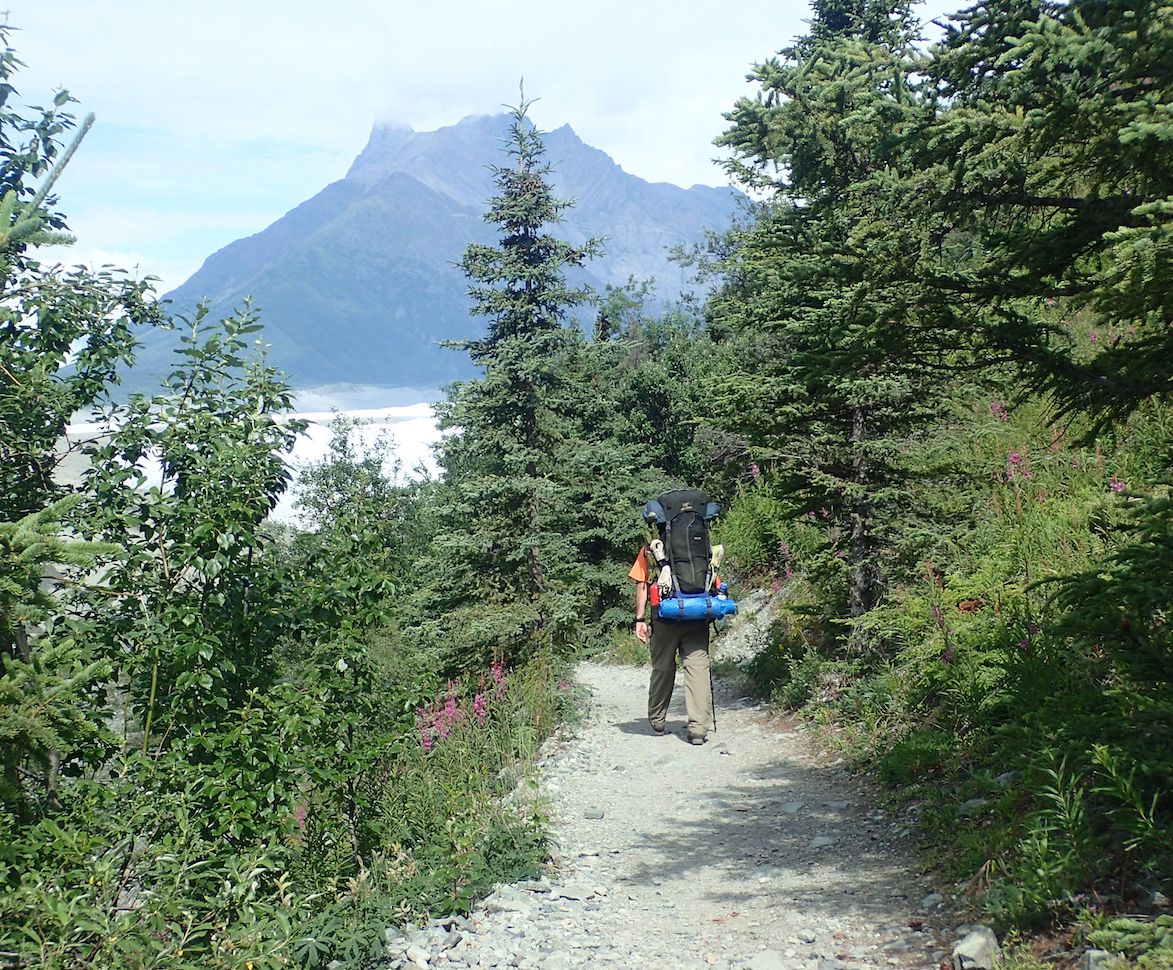 A man walking down a trail with a backpack.