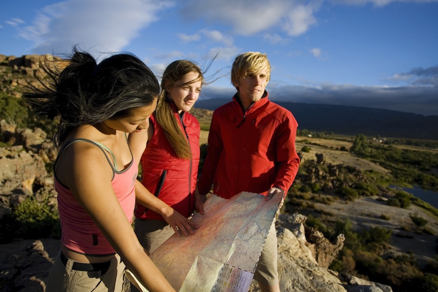 Three young people looking at a map on a rock.