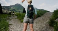 A woman standing on a gravel path with a backpack.