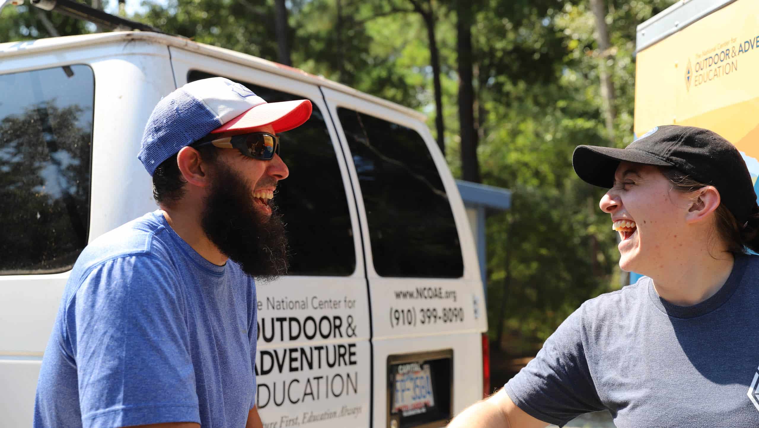 Two adults laughing next to an NCOAE van.