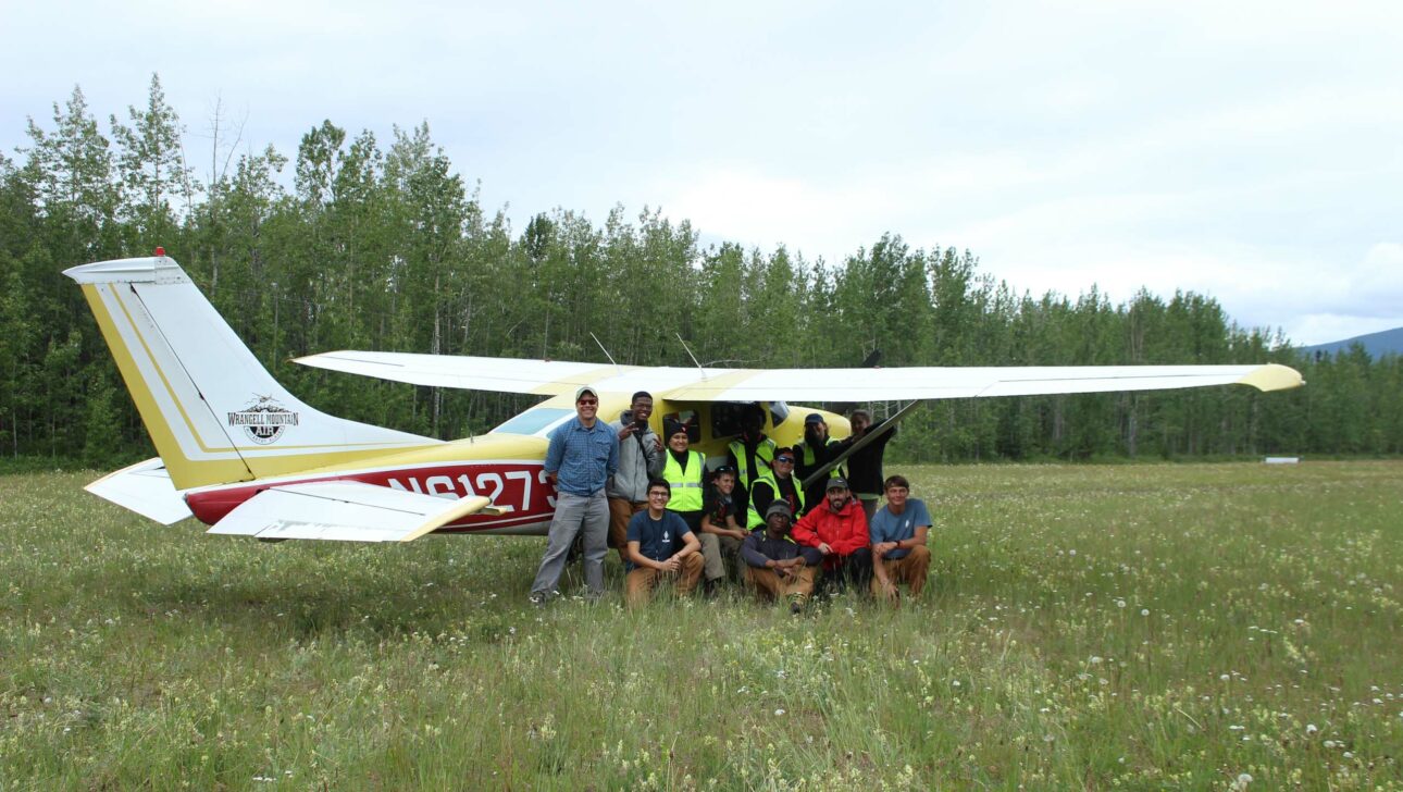 A group of people in front of an airplane in a field.