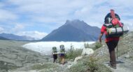 Three people backpacking in Alaska with a view of a mountain ahead of them.