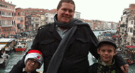 A man and two boys standing on a bridge in venice.