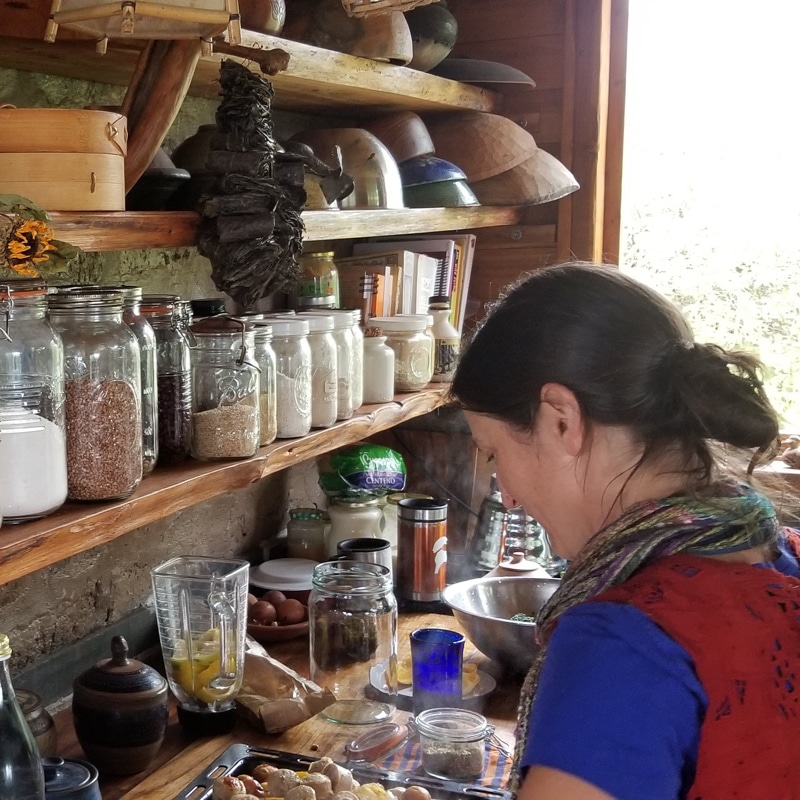 A woman cooking in a kitchen that has shelves filled with jars.