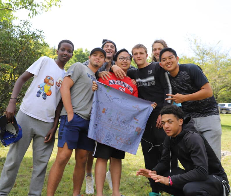A group of students holding a hand drawn fabric sign.