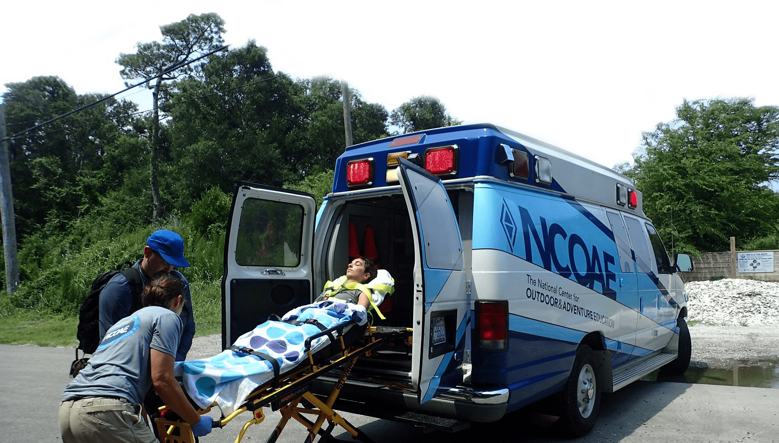 NCOAE EMT personnel pushing a patient on a stretcher into an NCOAE vehicle.