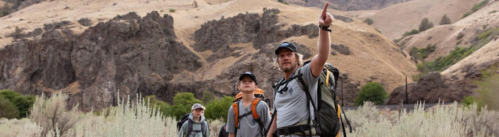 An NCOAE field instructor pointing forwards alongside two students.