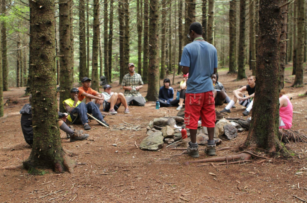 A group of students sitting together in a forest along with outdoor education instructors.