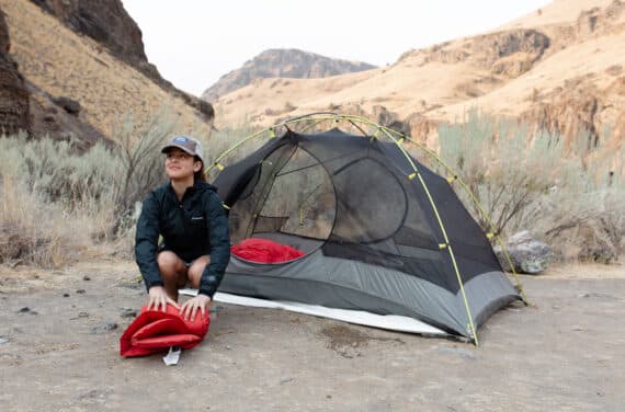 A student folding a sleeping bag in front of a tent.