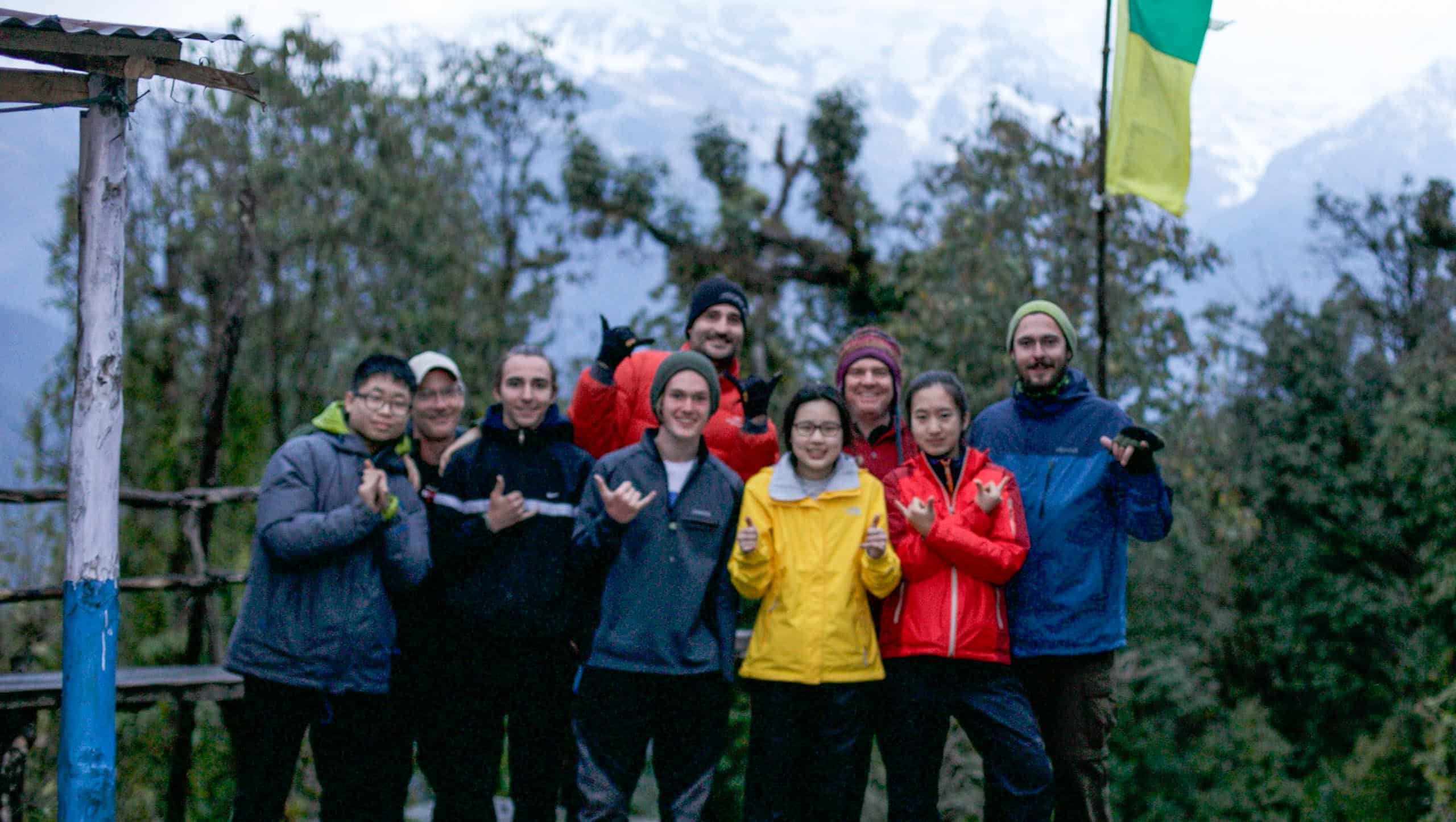 A group of people posing with a view of trees and snow capped mountains in the background.