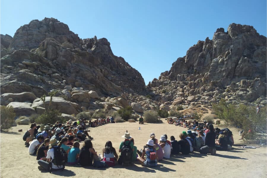 A group of people sitting in a circle with a rock mountains in the background.