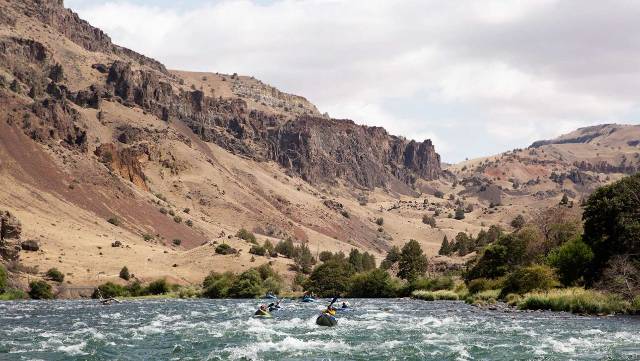 People kayaking in a river with mountains in the background.
