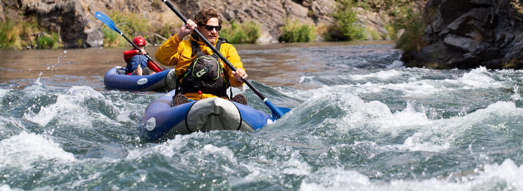 A man water rafting with another person following behind in another raft.