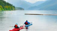 Two people kayaking on a lake with mountains in the background.