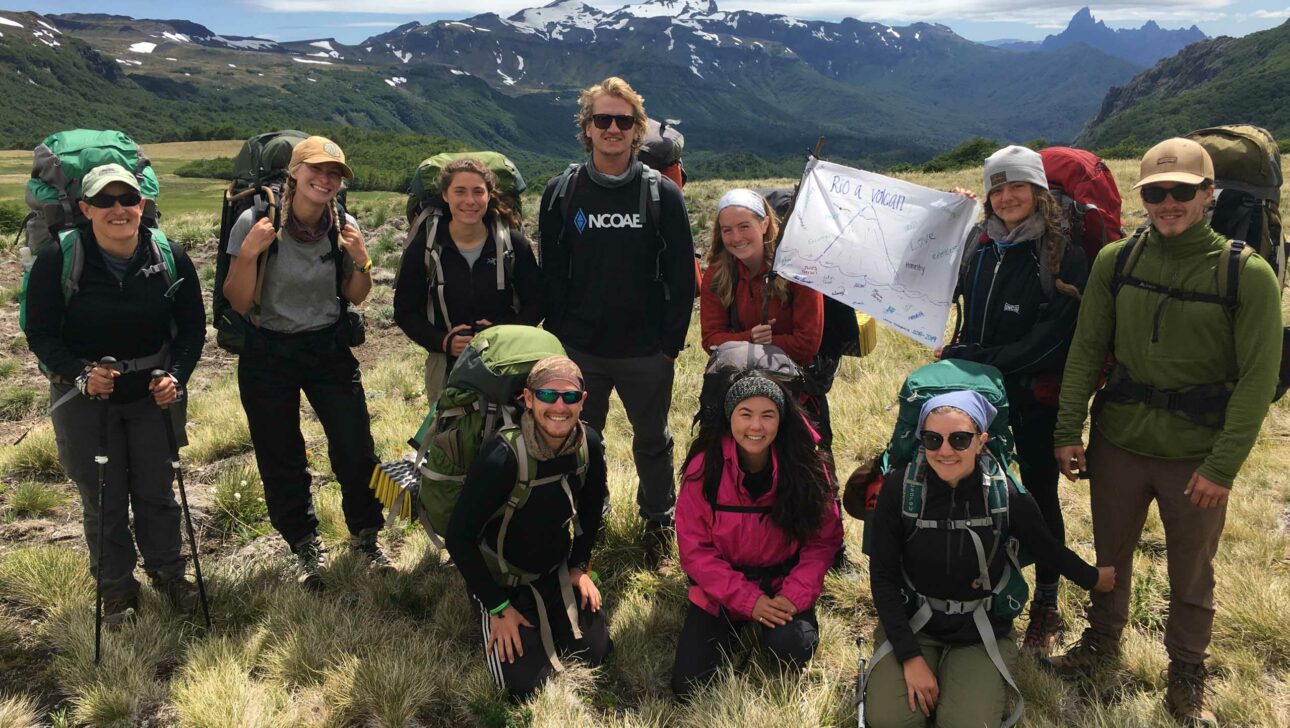 A group of people backpacking with a view of snowcapped mountains in the background.