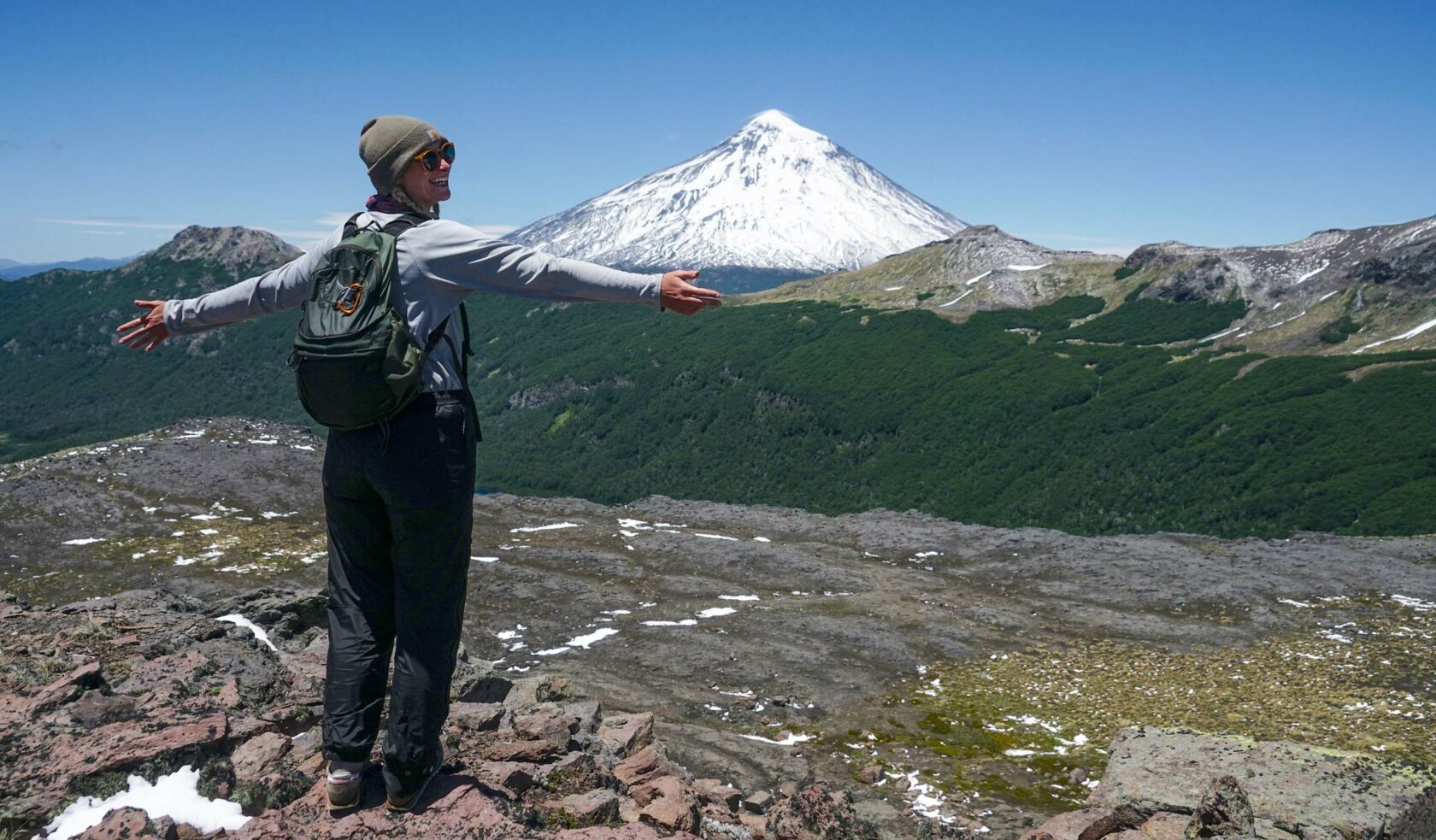 A woman with her arms outstretched, taking in a view of a snowcapped mountain.