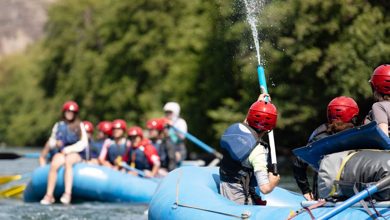 A student shooting a hose of water from a whitewater raft.