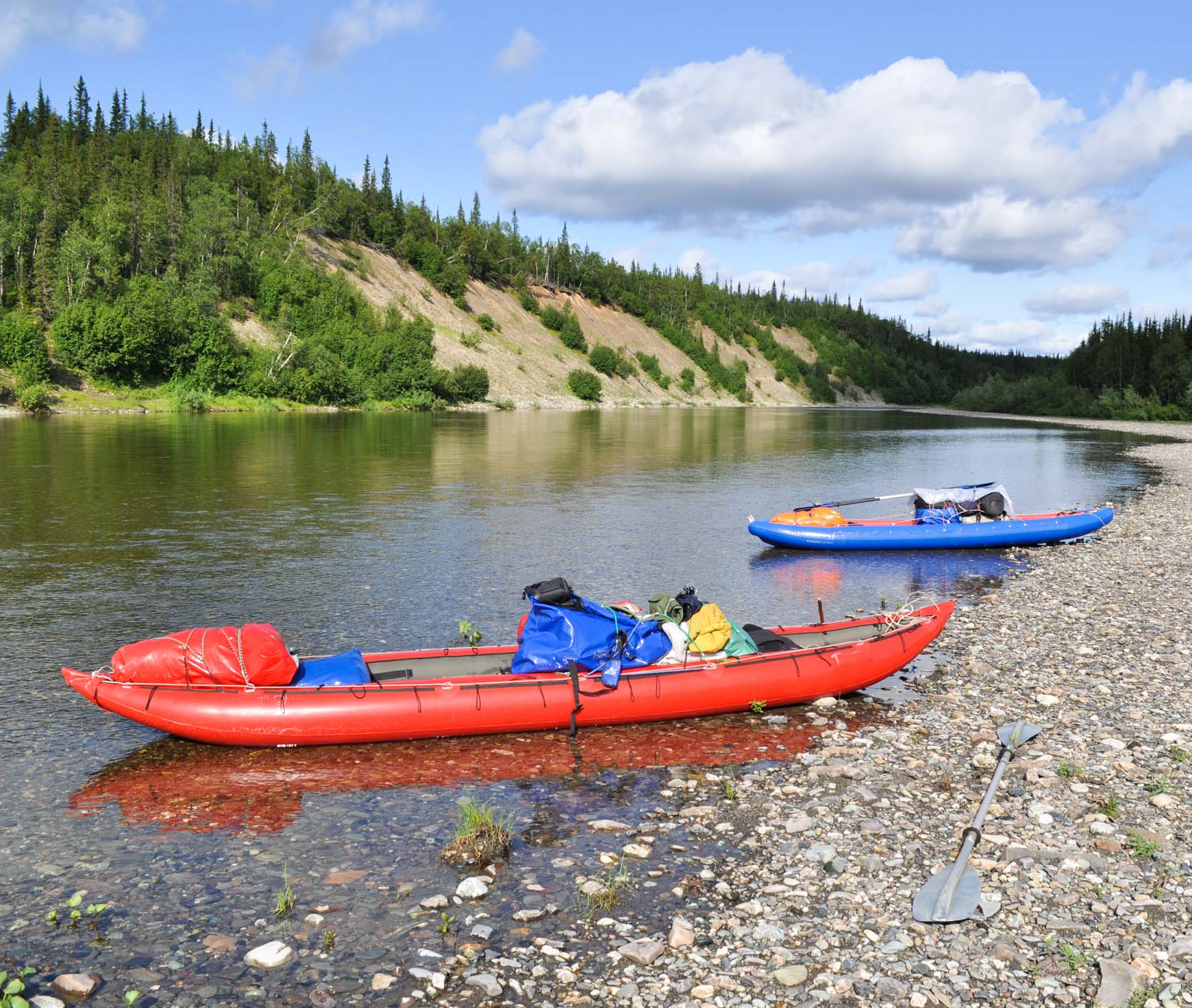 A red kayak and a blue kayak at the shore of a river.