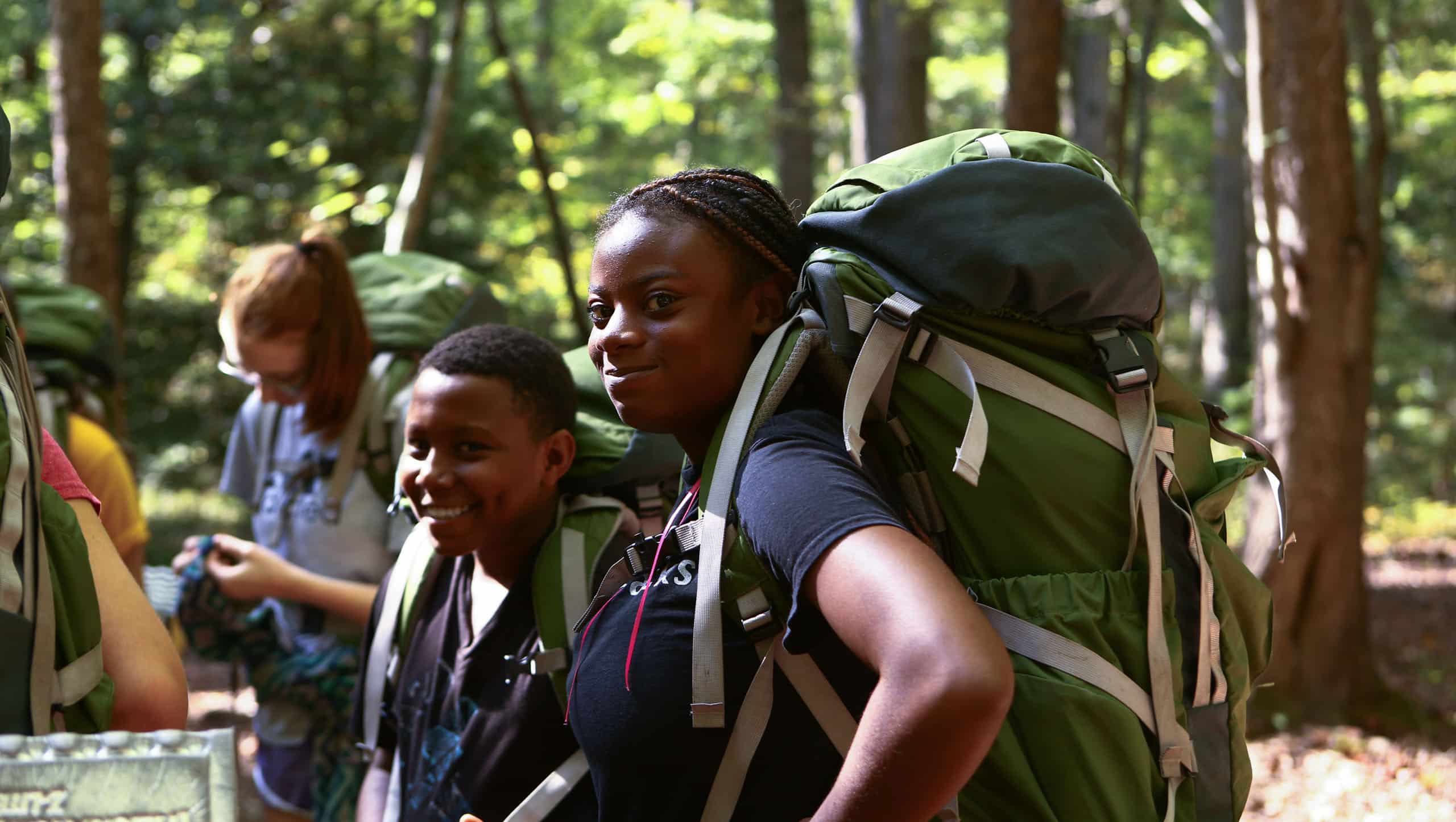 Two students with wearing hiking backpacks.