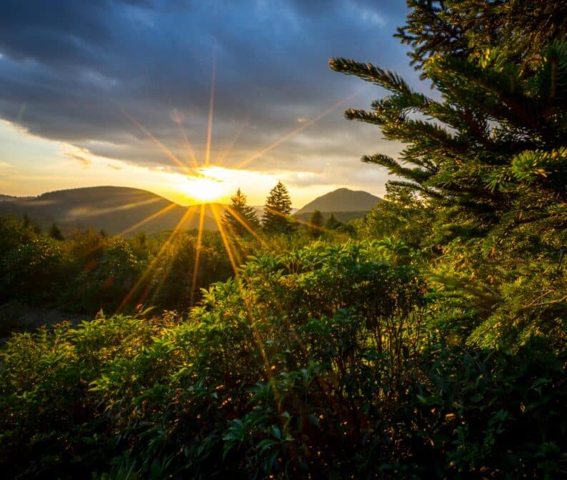 A view of the sun peeking out through the clouds and mountains.