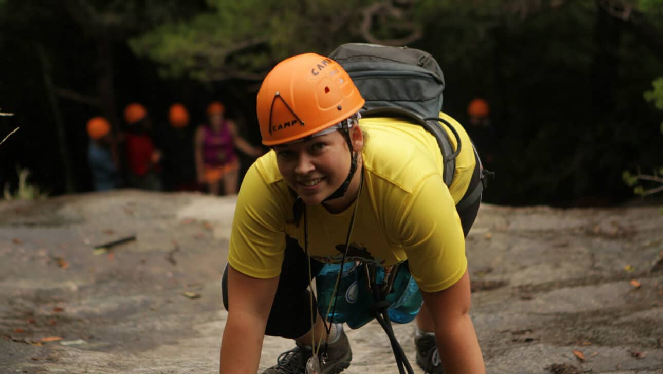 A student wearing an orange helmet rock climbing.