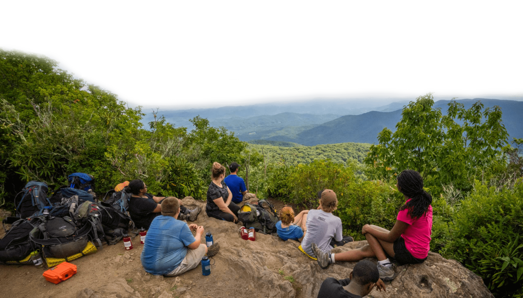 A group of teenagers sitting and enjoying a view of mountains.