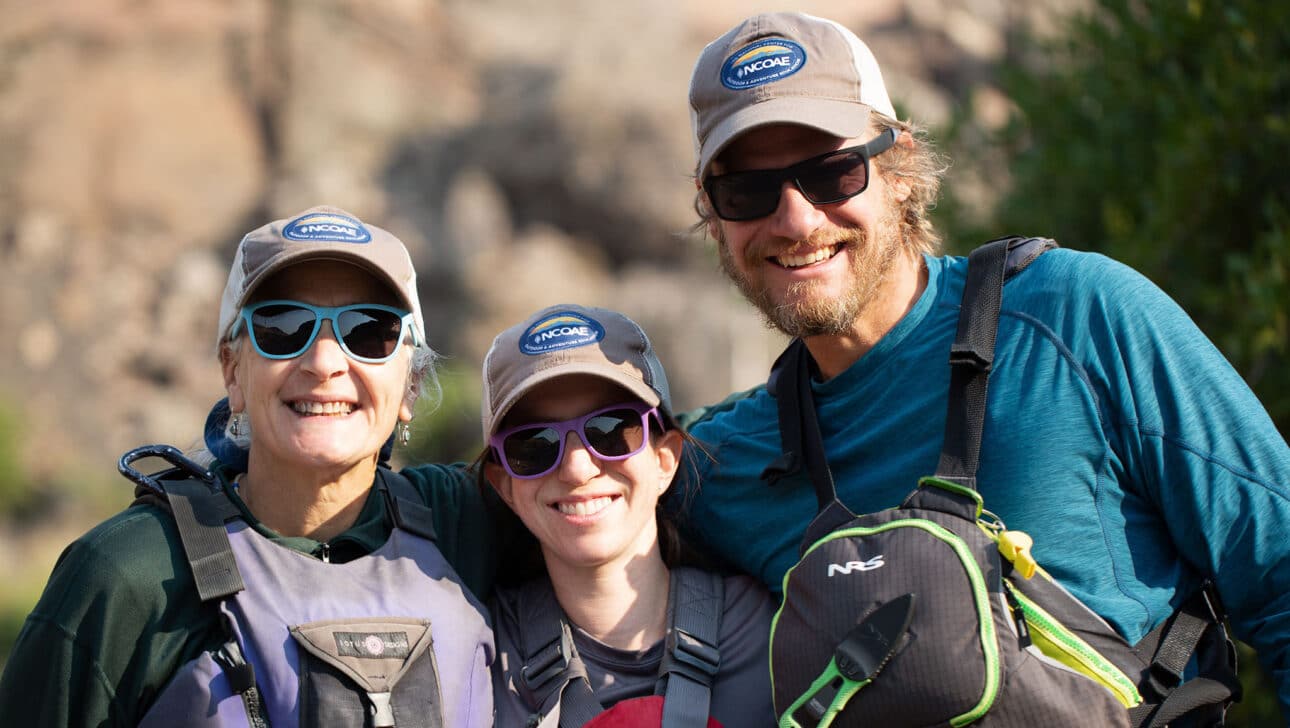 Three adults in sunglasses smiling.