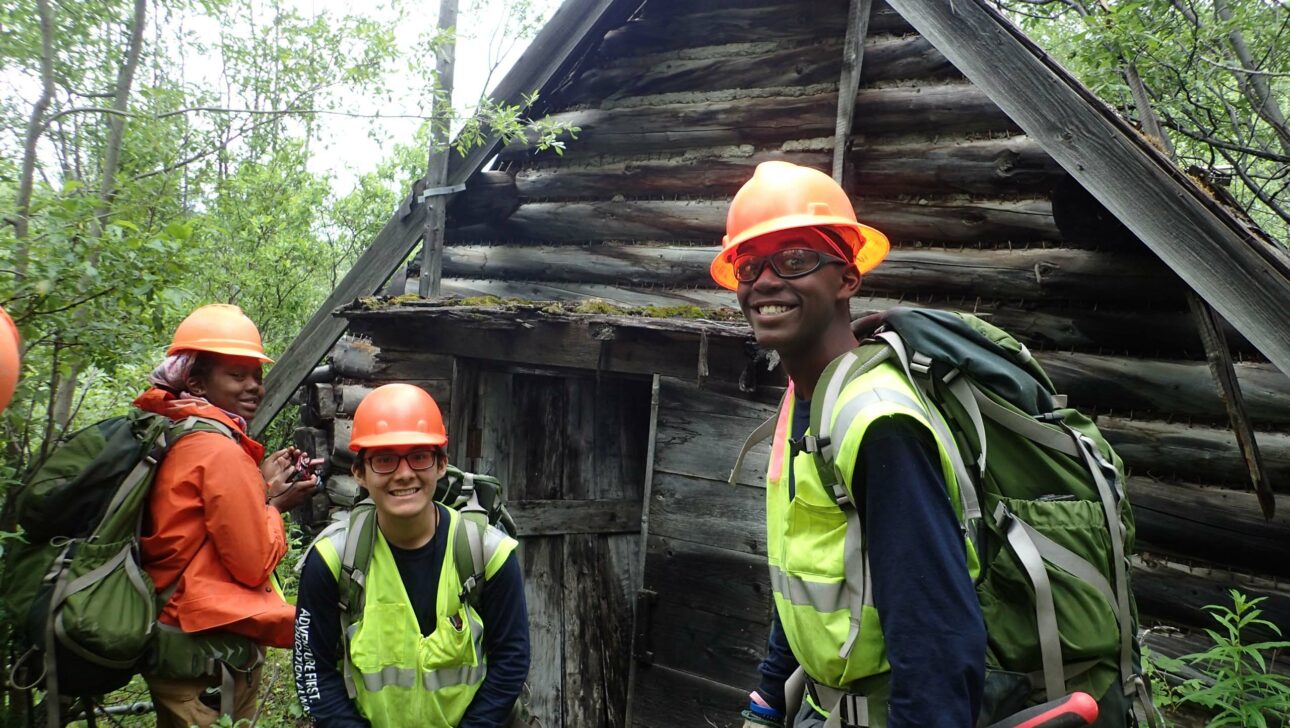 Three people in orange helmets and backpacking gear.