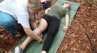 An NCOAE wilderness first aid student wrapping a bandage around a patient's leg.