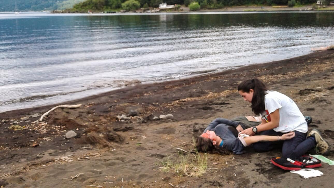 A wilderness medicine instructor treating a patient on a lake shore.
