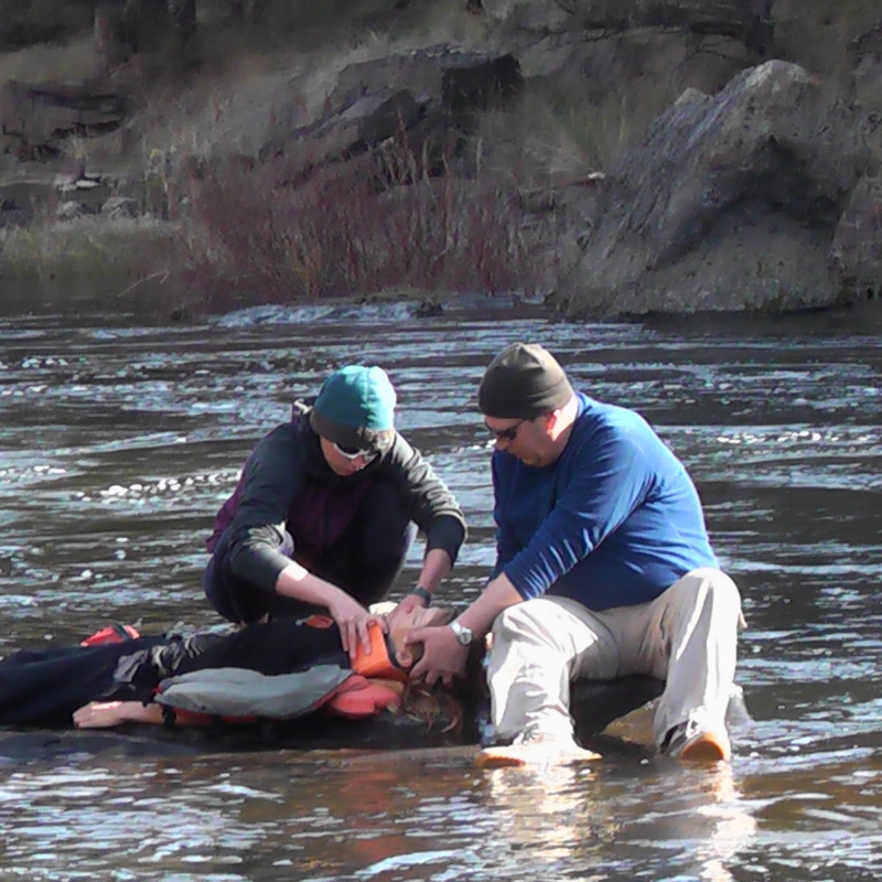 Two wilderness medicine personnel examining a patient in the middle of a river.