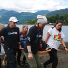 Wilderness Medicine personnel carrying a stretcher with a person away from a lake.