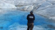 A person wearing an NCOAE t-shirt, standing in front of glaciers.