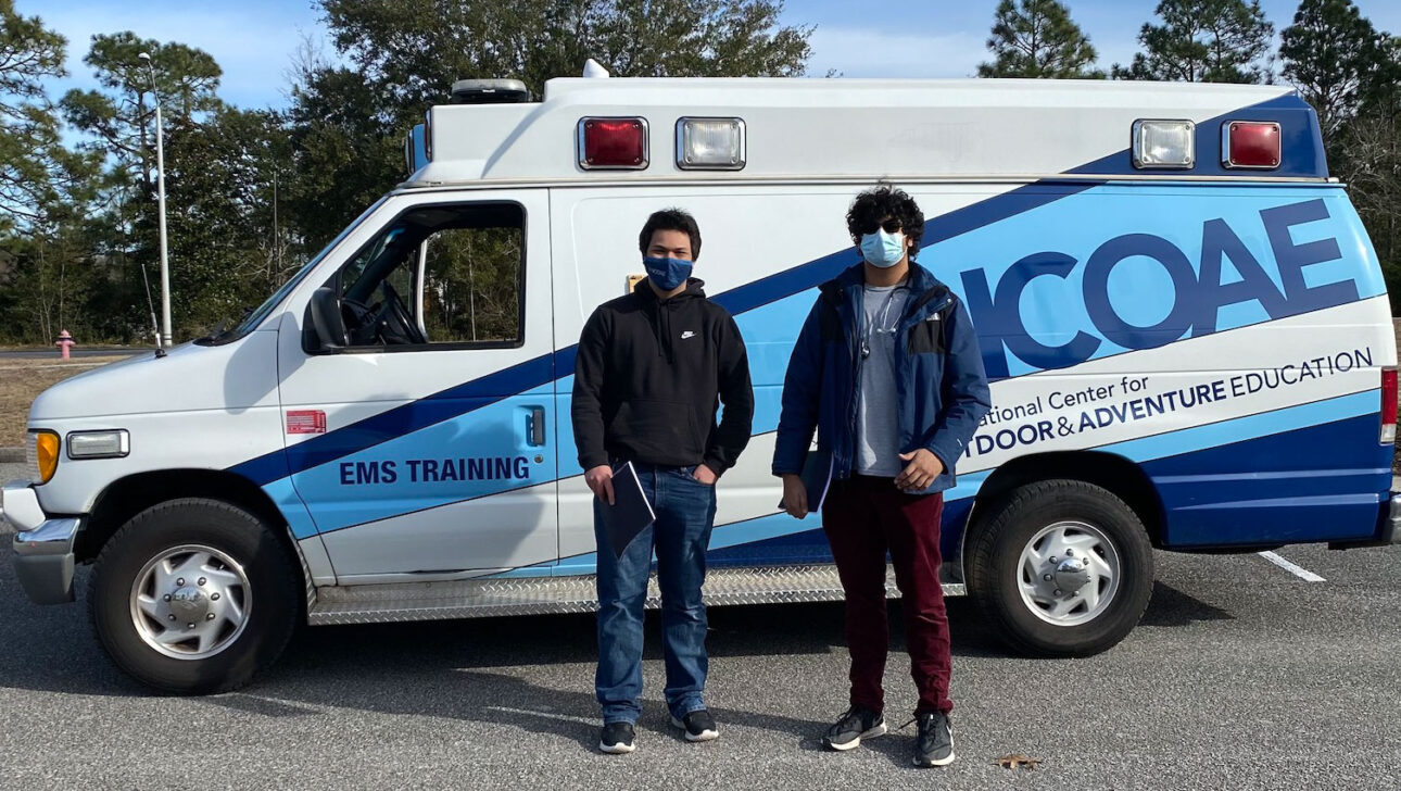Two EMT training students in front of an NCOAE vehicle.