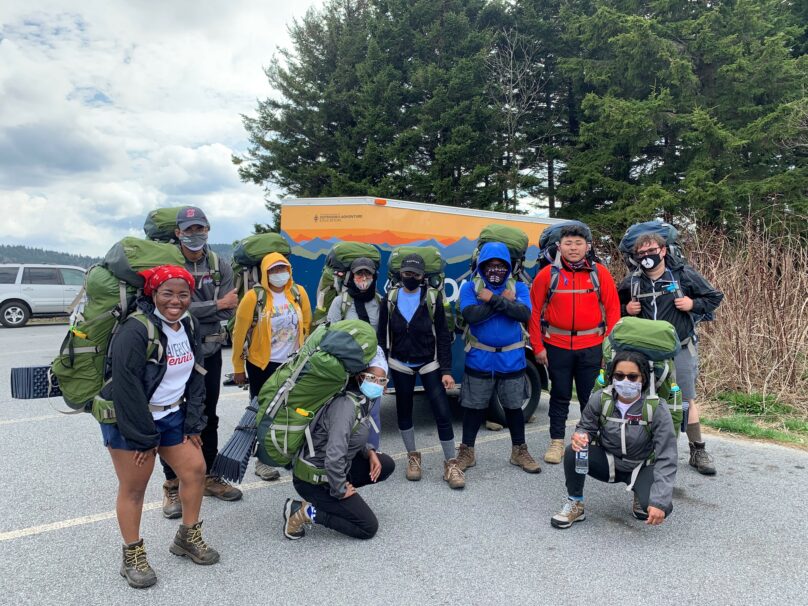 A group of people with backpacks posing in front of a van.