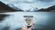 A person holding a coffee mug with mountains in the background.