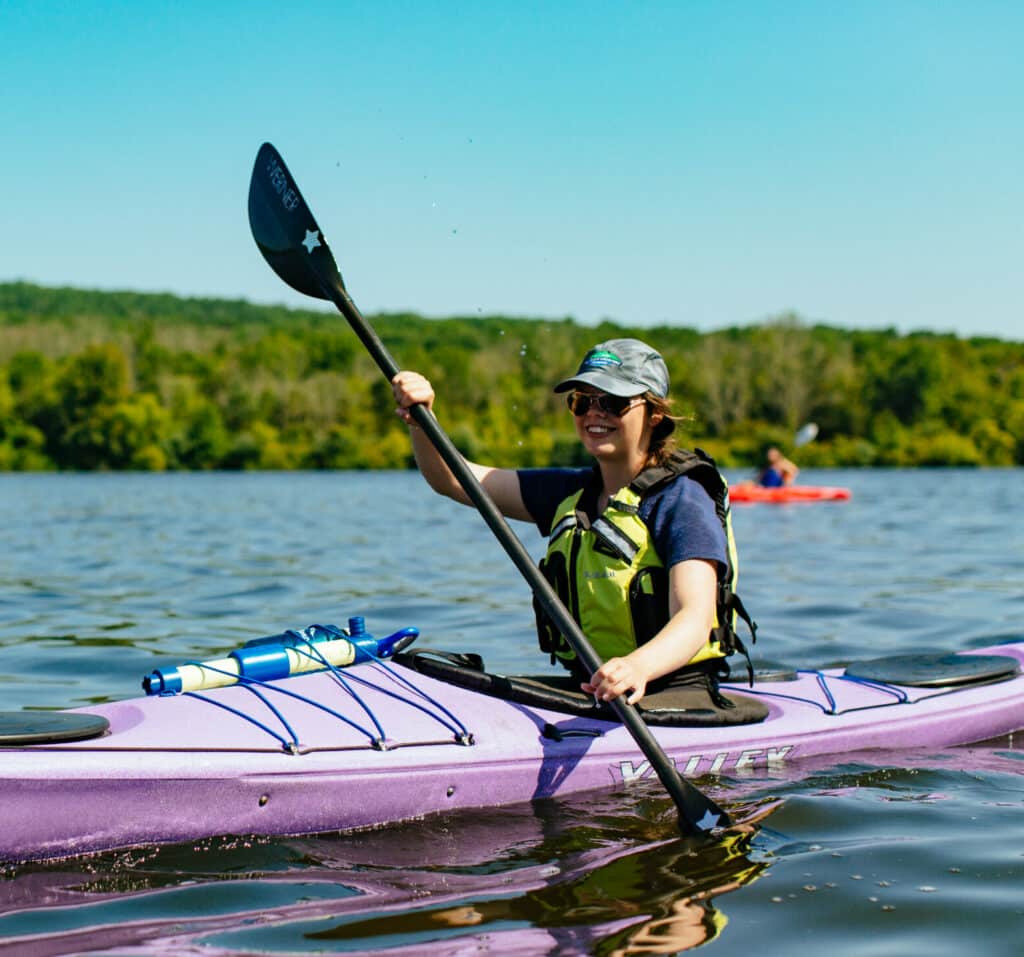 A woman paddles a purple kayak on a lake.