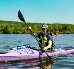A woman paddles a purple kayak on a lake.