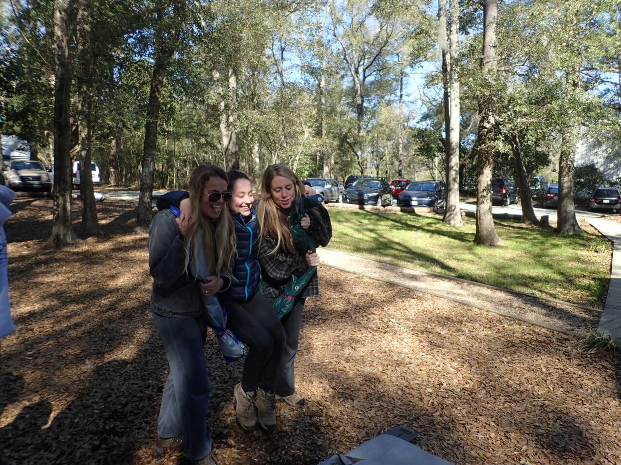 Three women standing in a wooded area.