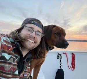 A man and his dog on a boat at sunset.