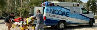 An ambulance is being loaded with a patient during an NCOAE EMT education course