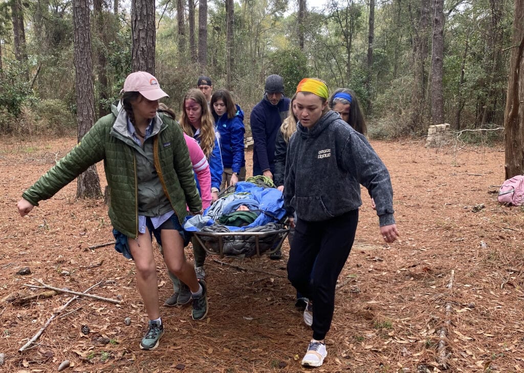 Group of NCOAE students carrying patient in stretcher during wilderness medicine course training