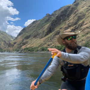 NCOAE staff member Kevin H paddling a boat with mountains in the background.