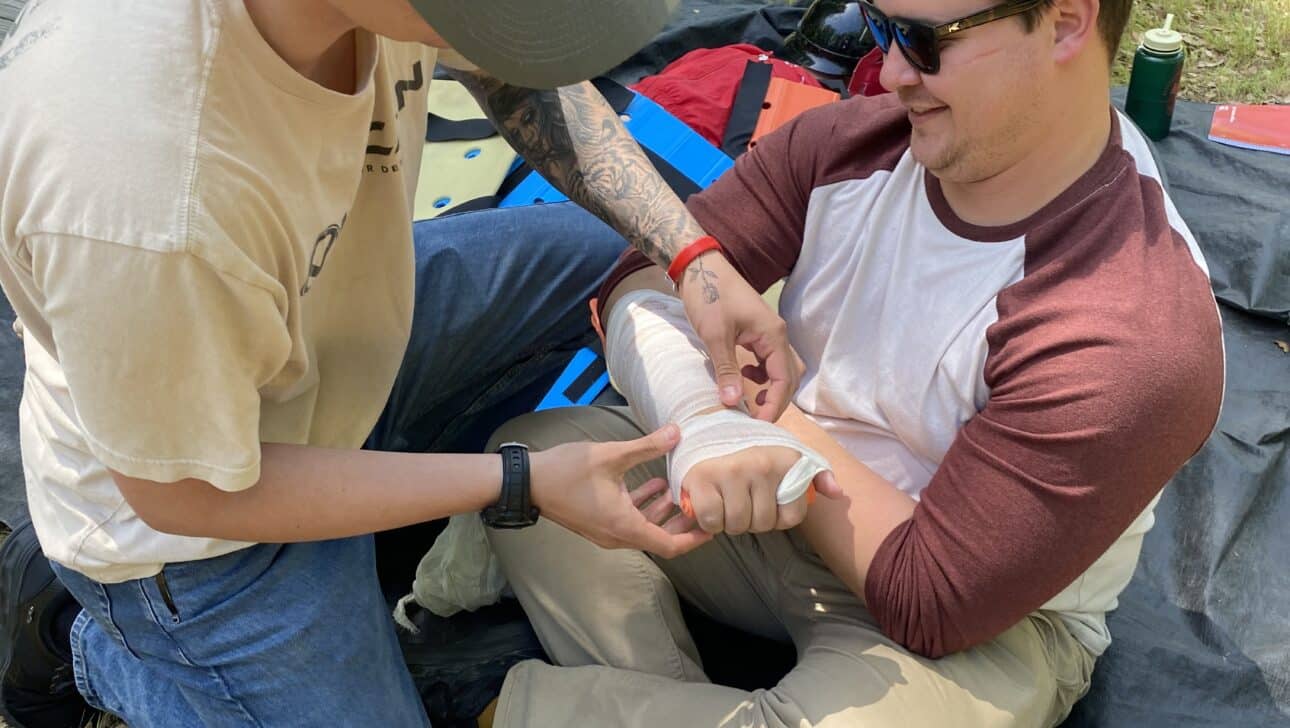 Two NCOAE students working on a makeshift arm bandage during an Intensive EMT training