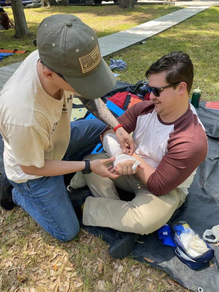 Two NCOAE students working on a makeshift arm bandage during an Intensive EMT training